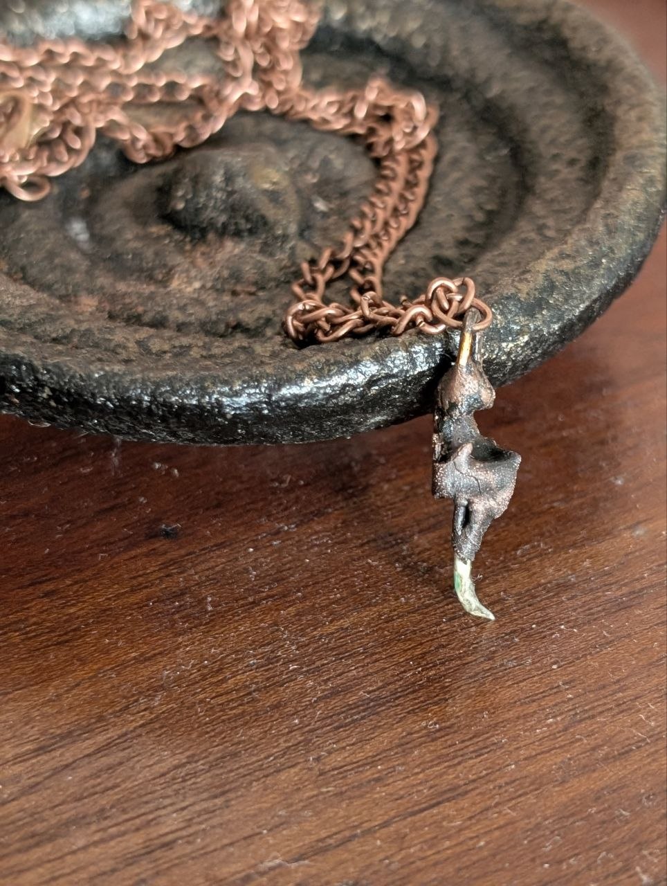 Copper-plated rattlesnake fang pendant hanging in front of a dark dish