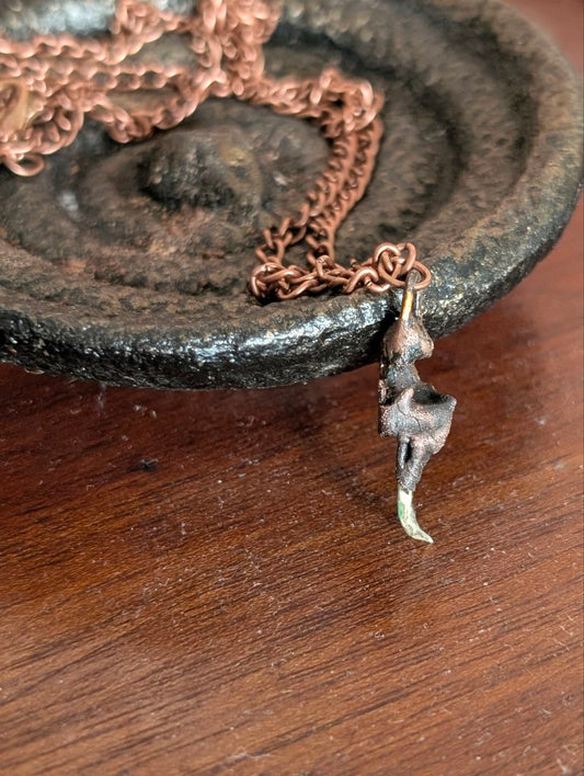 Copper-plated rattlesnake fang pendant hanging in front of a dark dish