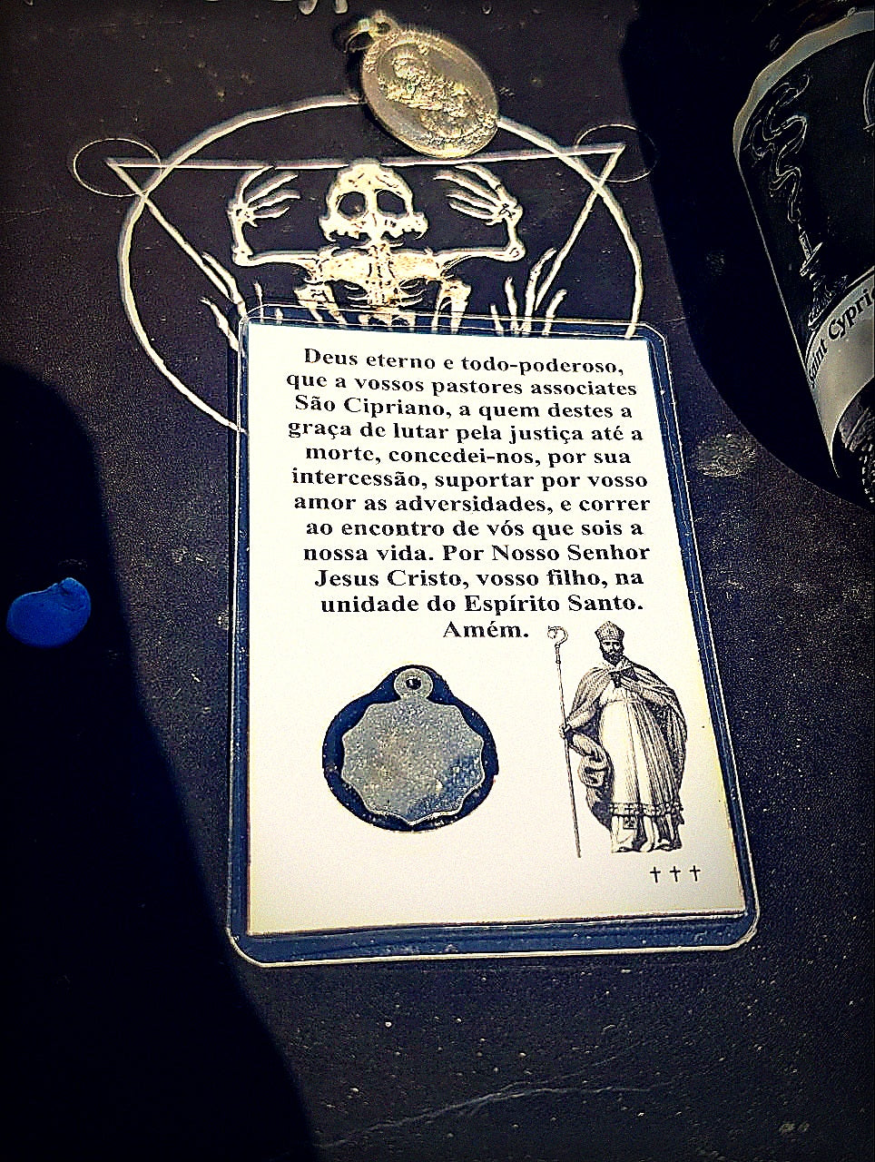 Back of Saint Cyprian prayer card with medal in moody altar light