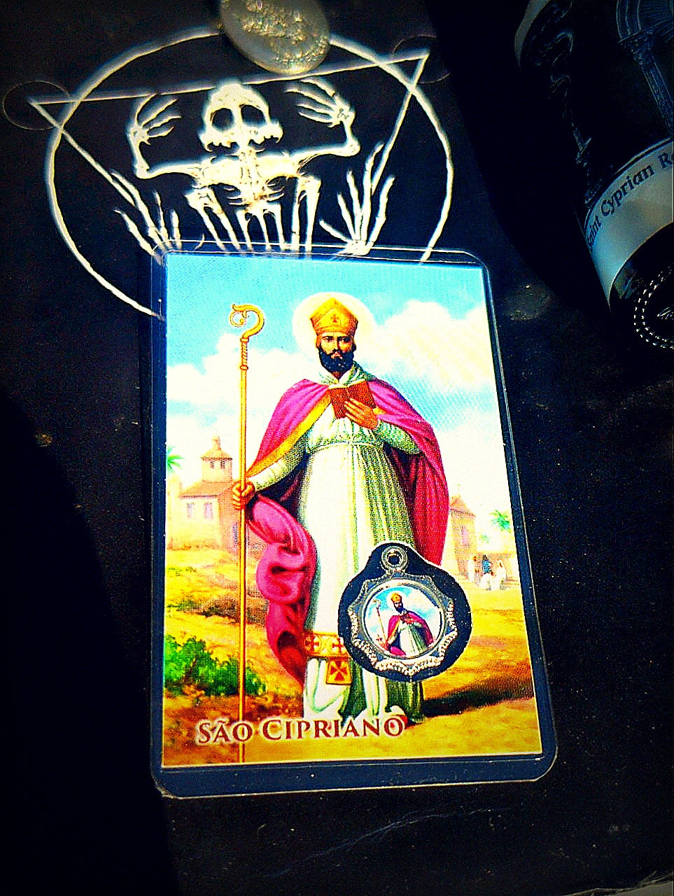 Saint Cyprian prayer card, medal, and relic ritual oil in dark devotional setting