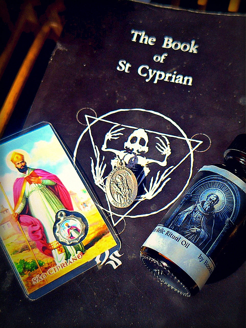 Edgy dark Saint Cyprian bundle product photo with prayer card, oil bottle, medal, and book